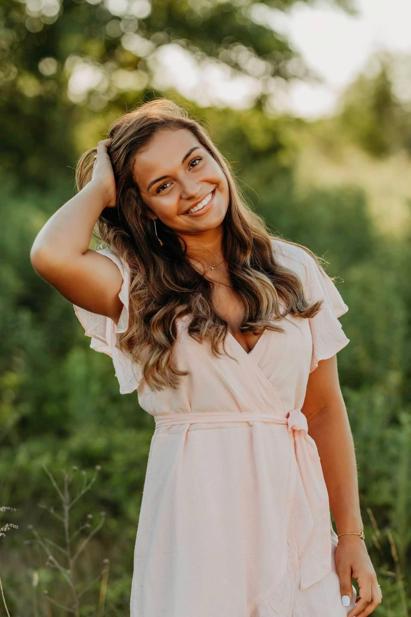 A student poses in front of lush green backdrop smiling.